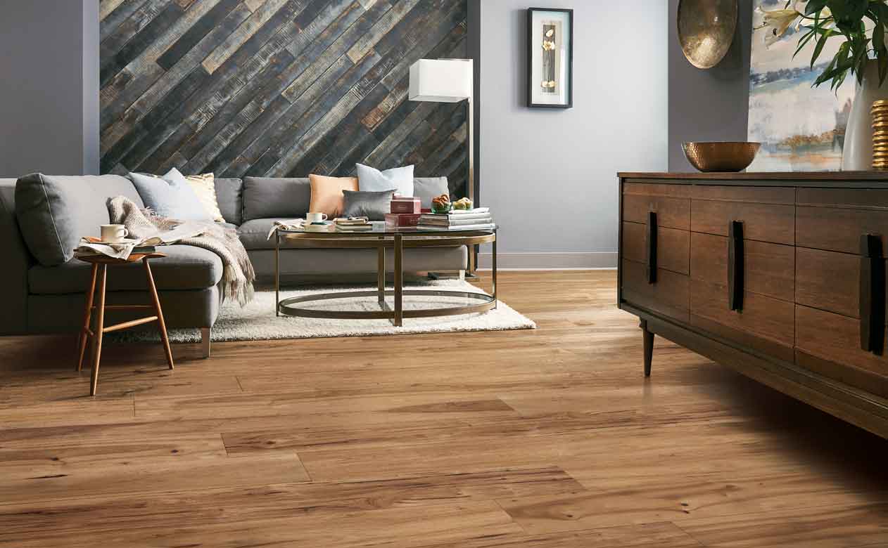 honey-hued Hardwood Flooring in Living Room with cozy layered gray couch, vintage plank accent wall and white area rug under coffee table